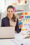 Portrait of happy fashion designer with credit card in office