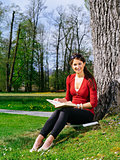 Woman reading and sitting against a tree