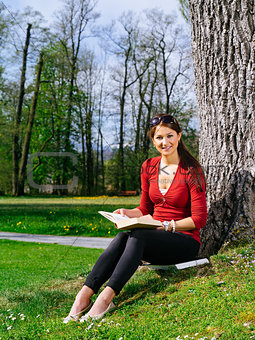 Woman reading and sitting against a tree