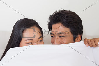 Happy couple holding duvet over face