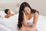 Woman sitting on bed holding pregnancy test as boyfriend sleeps