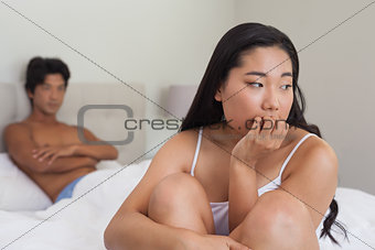Boyfriend looking at upset girlfriend sitting on end of bed