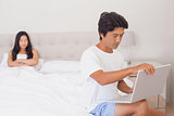 Woman watching boyfriend using laptop on end of bed