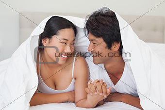 Happy couple lying on bed together under the duvet
