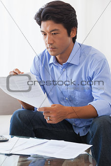 Serious man sitting on couch paying his bills