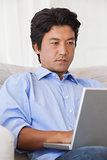 Serious man sitting on couch using laptop