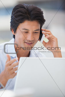 Happy man using his laptop talking on the phone