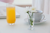 White flower in a vase with coffee and orange juice on table