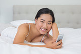 Smiling asian woman lying on bed sending a text
