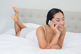 Smiling asian woman lying on bed talking on phone