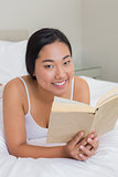 Smiling woman lying on bed reading
