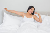 Smiling woman lying in bed stretching in the morning