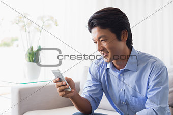 Happy man sitting on couch texting on phone