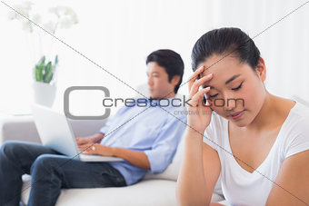 Upset woman sitting on couch while boyfriend uses laptop