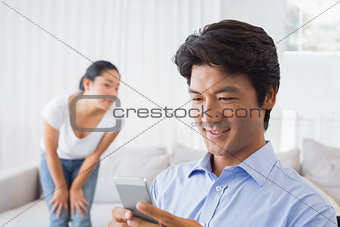 Man sending a text while girlfriend watches from couch