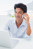 Smiling man using his laptop and talking on phone