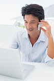 Smiling man using his laptop and talking on phone