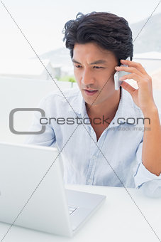 Serious man using his laptop and talking on phone