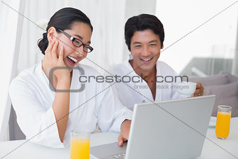 Couple in bathrobes spending the morning together using laptop