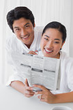 Couple in bathrobes reading newspaper together in the morning