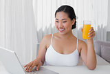 Happy woman using laptop and having orange juice