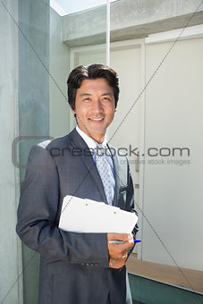 Confident estate agent standing at front door with clipboard