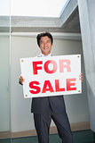 Confident estate agent standing at front door showing for sale sign