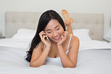 Shocked woman lying on bed talking on the phone