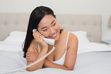 Happy woman lying on bed talking on the land line