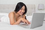 Happy woman lying on bed using laptop