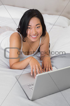 Happy woman lying on bed using laptop