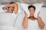 Annoyed woman covering her ears with pillows to block out snoring