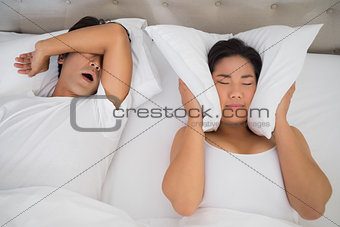 Annoyed woman covering her ears with pillows to block out snoring