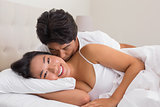 Man kissing his girlfriend on the cheek in bed