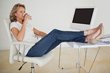 Casual businesswoman having a coffee with her feet up at desk