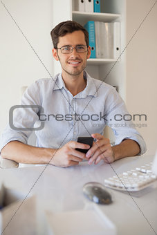 Casual businessman sending a text at his desk