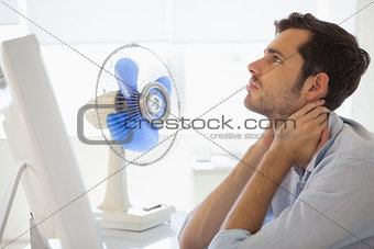 Casual businessman sitting at desk with electric fan