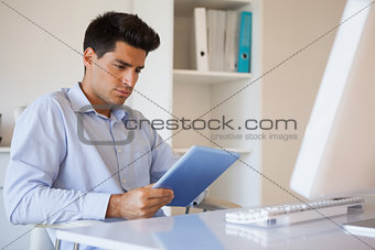 Casual businessman using his tablet at his desk