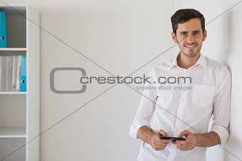 Casual businessman leaning against wall sending a text