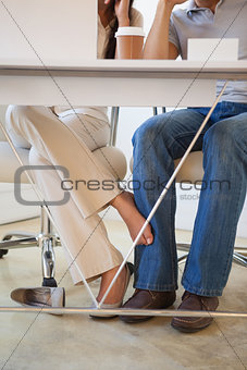 Casual businesswoman playing footsie with colleague under desk