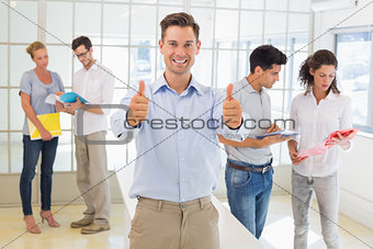 Casual boss giving thumbs up at camera in front of business team