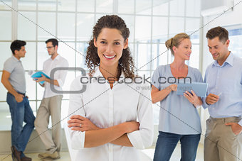 Casual businesswoman smiling at camera with team behind her