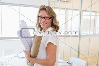 Casual architect smiling at camera holding blueprints