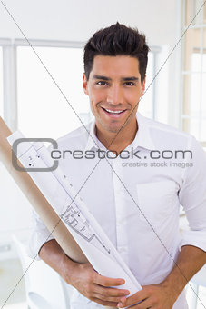 Casual handsome architect smiling at camera holding blueprint