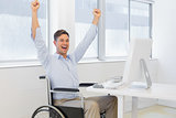 Casual businessman in wheelchair cheering at his desk