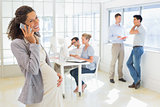 Pregnant businesswoman talking on phone with team behind her