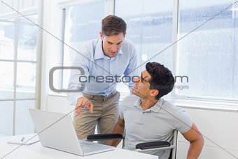 Casual businessman in wheelchair talking with colleague using laptop