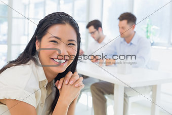 Casual businesswoman smiling at camera with team behind her