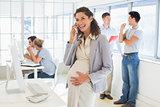 Pregnant businesswoman talking on phone with team behind her