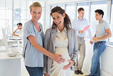 Casual businesswoman touching her pregnant colleagues belly